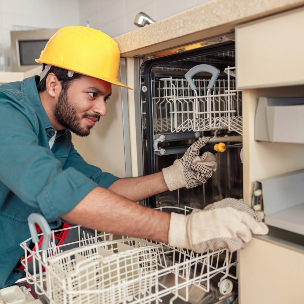 Focused handyman in special clothing repairing dishwasher in modern kitchen Focused handyman in special clothing repairing dishwasher in modern kitchen