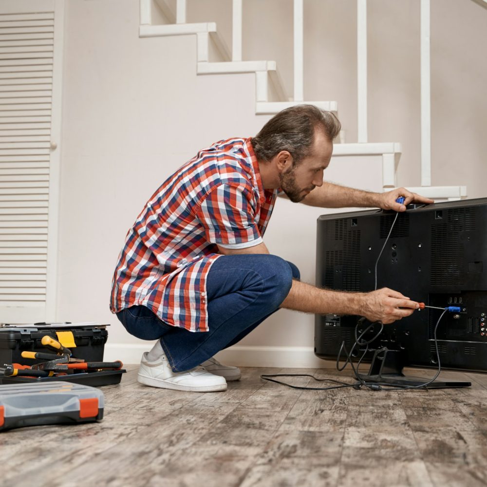 Young caucasian service man fixing tv set Young caucasian service man fixing tv set