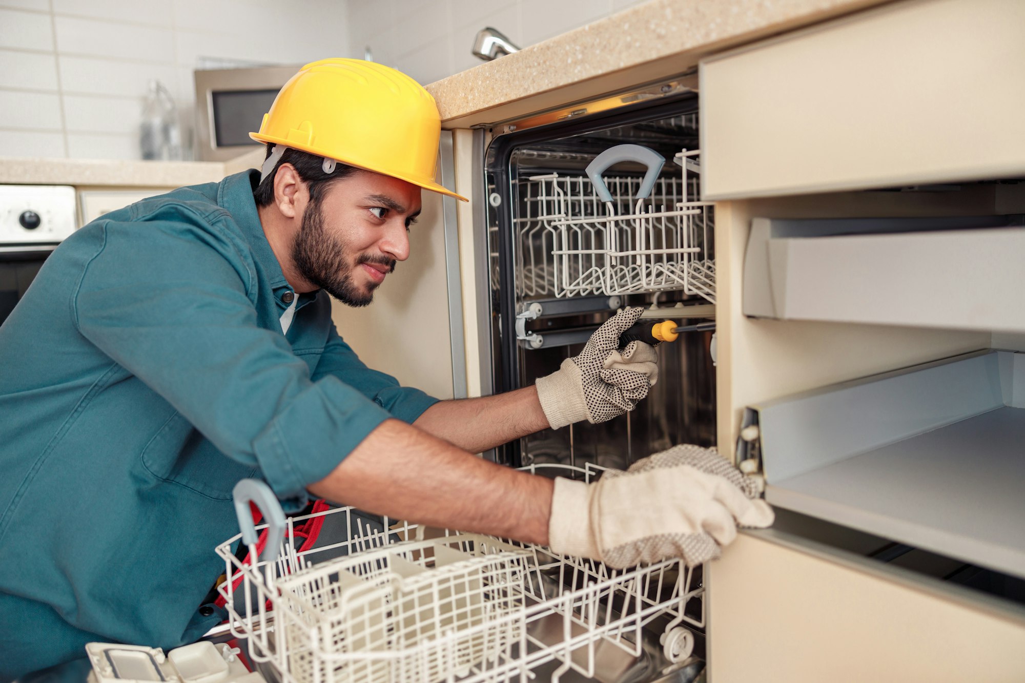 Focused handyman in special clothing repairing dishwasher in modern kitchen